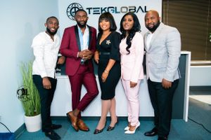 Professional group photo of business team in formal attire outside office building with Tekglobal sign.