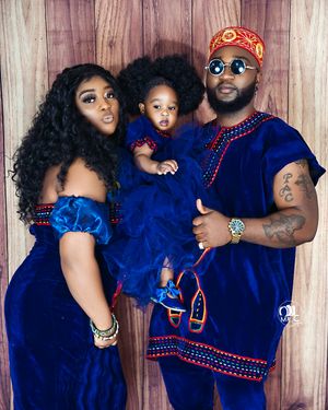 Family in coordinated royal blue traditional outfits with decorative red trim pose against wooden backdrop.