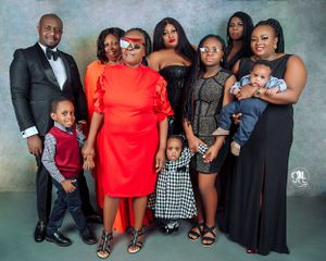 Formal family portrait with members wearing elegant black, red and formal attire against gray backdrop.