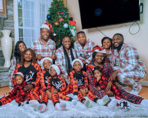 Large family group wearing matching buffalo plaid pajamas pose by Christmas tree for holiday photo.