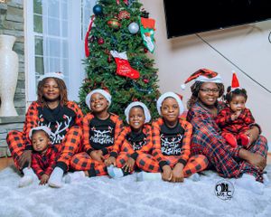 Holiday family photo with children in matching buffalo plaid pajamas by Christmas tree.