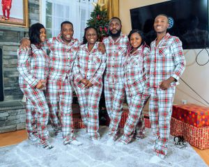 Family group wearing matching red plaid holiday pajamas posing in front of fireplace.