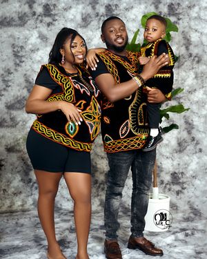 Family wearing matching African print outfits poses together against gray backdrop.