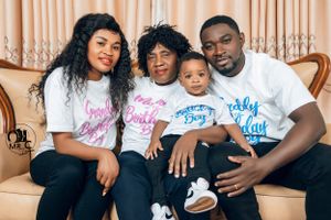Family group wearing matching t-shirts poses together on beige couch for portrait.