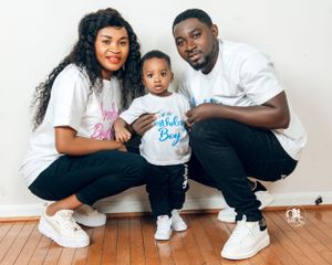 Family wearing coordinated white t-shirts with blue and pink text poses together on hardwood floor.
