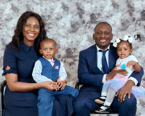 Family portrait with parents and two young children in formal attire against a textured gray background.