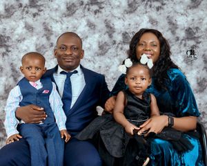 Family of four in coordinated formal wear poses for a portrait against a mottled gray background.