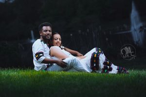 Couple in white outfits laying together on grass during an outdoor photoshoot.