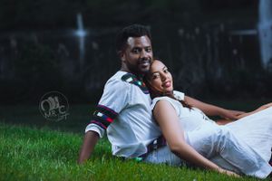 Romantic couple pose together on grass during outdoor photography session.