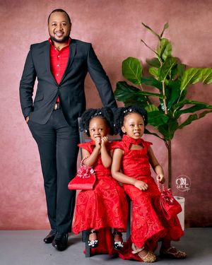 Family portrait with black suit and matching red dresses against pink backdrop with plant.
