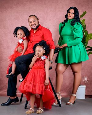 Stylish family portrait with matching red and green outfits against pink backdrop with plant.