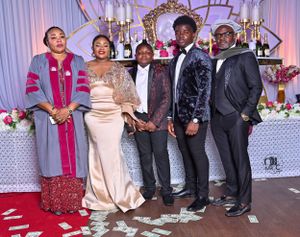 Formal event photo with group in elegant attire posing by decorated table with candelabras.