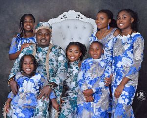 Family portrait in coordinated blue and white floral outfits with ornate white throne chair.