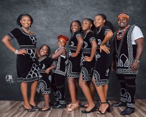 Family portrait in coordinated black and white traditional outfits against dark background.