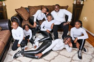 A family in matching white outfits poses casually together on a carpeted floor.
