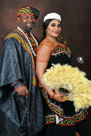 Elegant couple in traditional African formal wear with yellow feather fan and colorful embroidery.