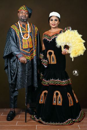 Couple in traditional African attire with yellow feather fan and elegant embroidered details.