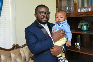Indoor portrait of a parent and baby in formal attire sitting on leather furniture.
