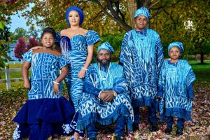 Family wearing coordinated blue African print outfits poses outdoors among fall foliage.