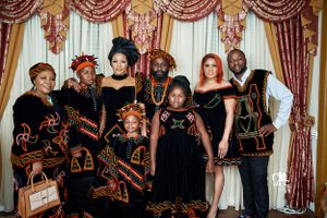 Group photo of people wearing coordinated black and gold traditional African attire against elegant curtained backdrop.