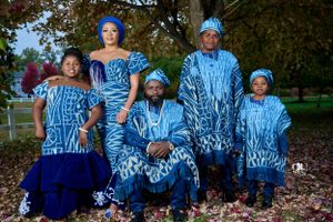 Family group wearing matching blue and white traditional African prints poses outdoors in autumn setting.