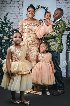 A family portrait with coordinated formal attire in gold and pink against a white brick backdrop.