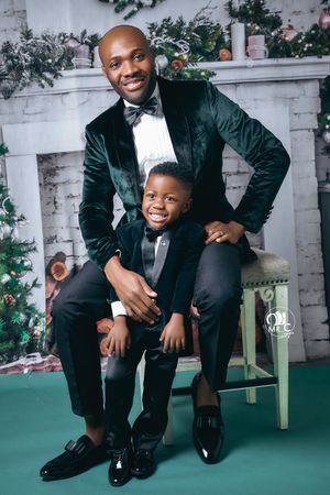 Holiday portrait in matching green velvet suits posed in front of decorated Christmas fireplace.
