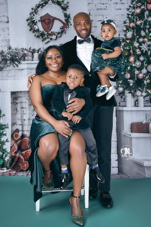 Holiday family portrait in front of decorated Christmas fireplace wearing formal velvet attire.