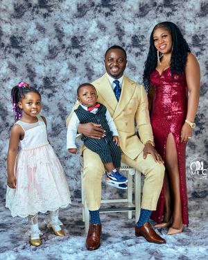 Family portrait with coordinated formal attire including gold suit and red gown against textured backdrop.