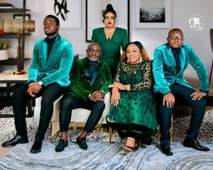 Group photo of five people wearing coordinated emerald green and black formal attire in modern interior.