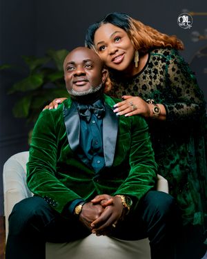 Stylish couple in green velvet and black lace formal wear pose for romantic studio portrait.