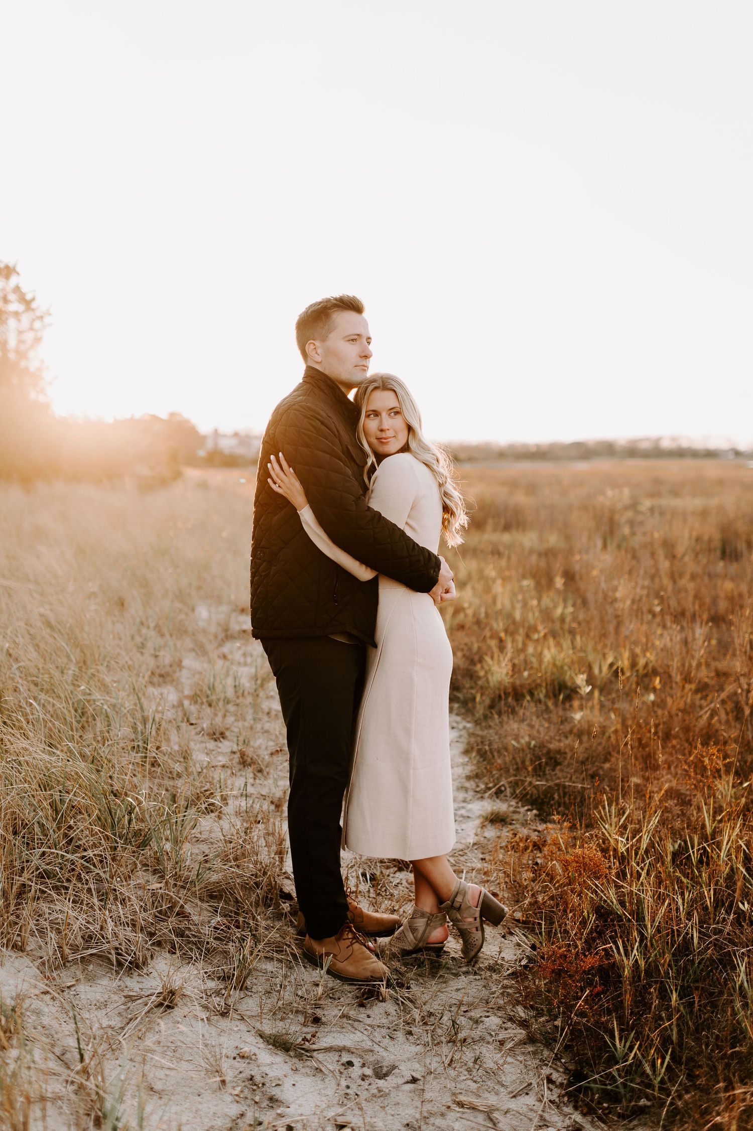 A couple shares a tender embrace among dried grass during sunset.
