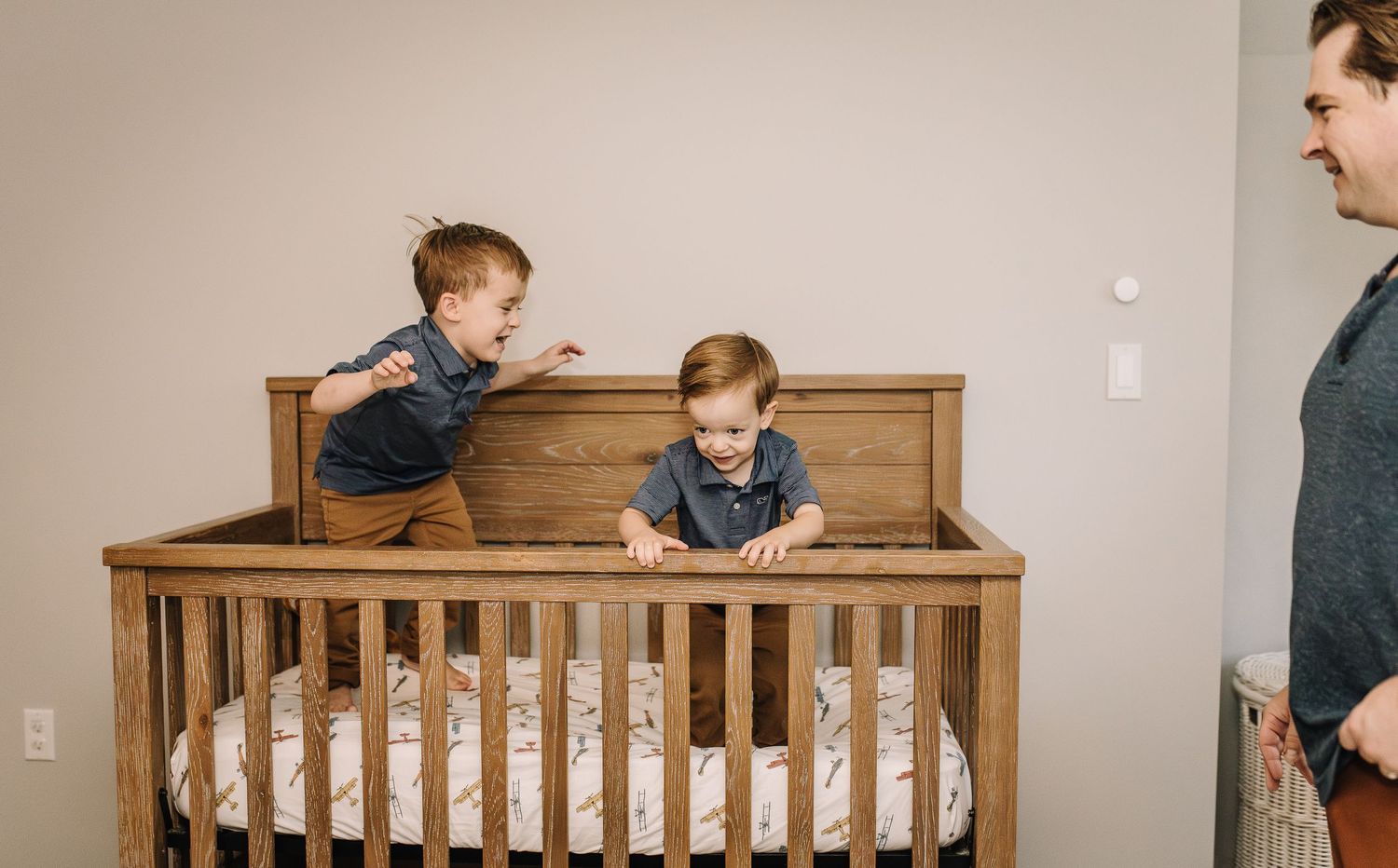 Two children playing and climbing on a wooden crib in a bedroom.