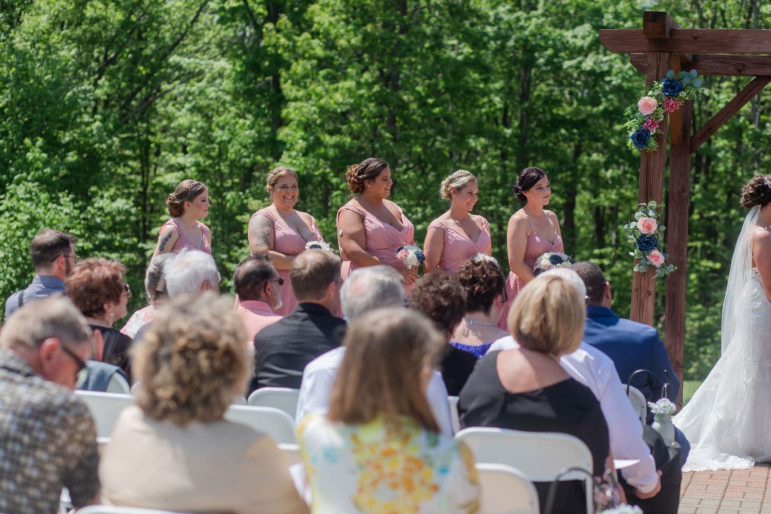 Guests seated in white chairs at an outdoor wedding ceremony surrounded by lush greenery.