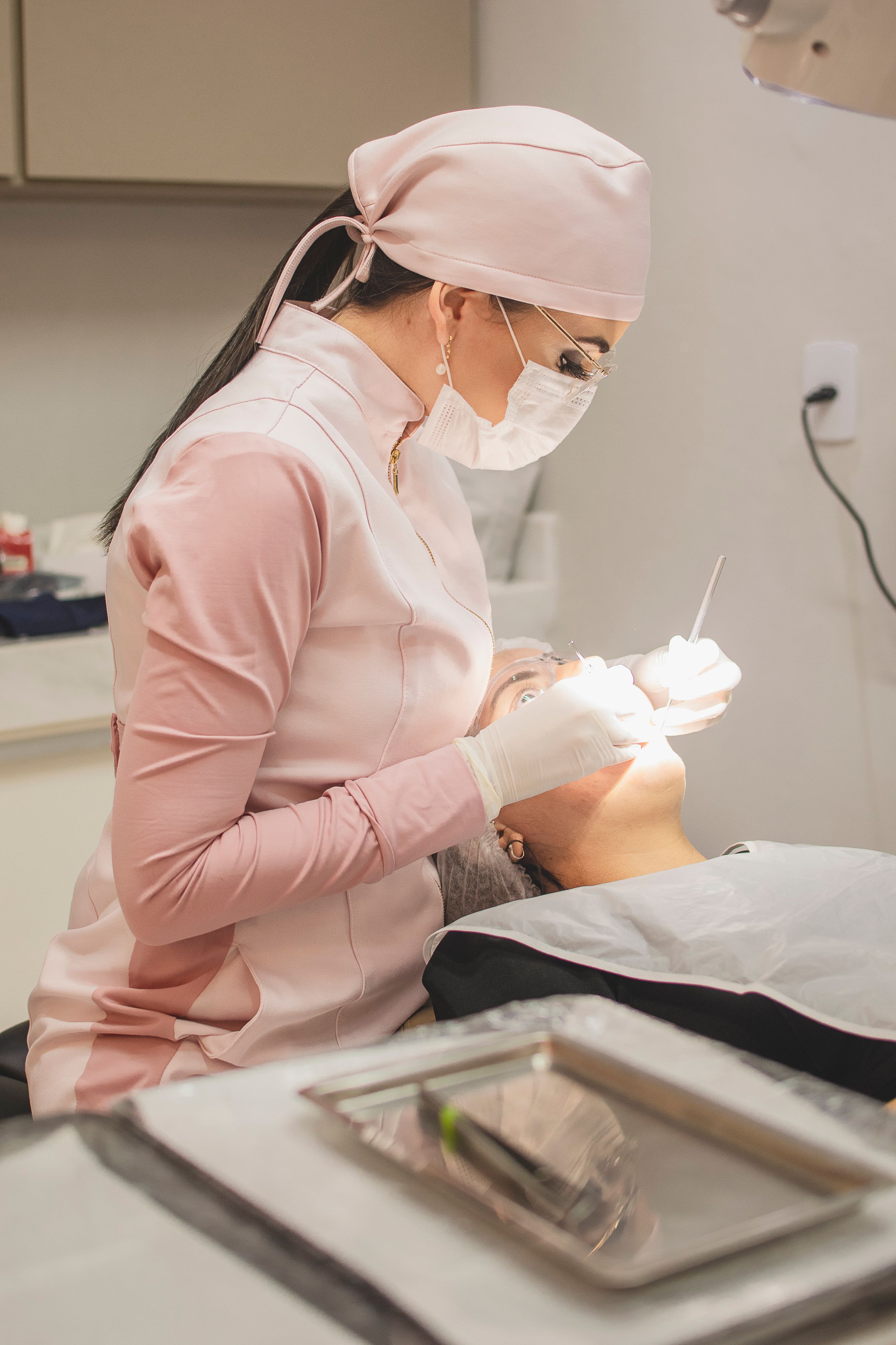 Dental professional in pink attire performing a dental procedure in a clinical setting.