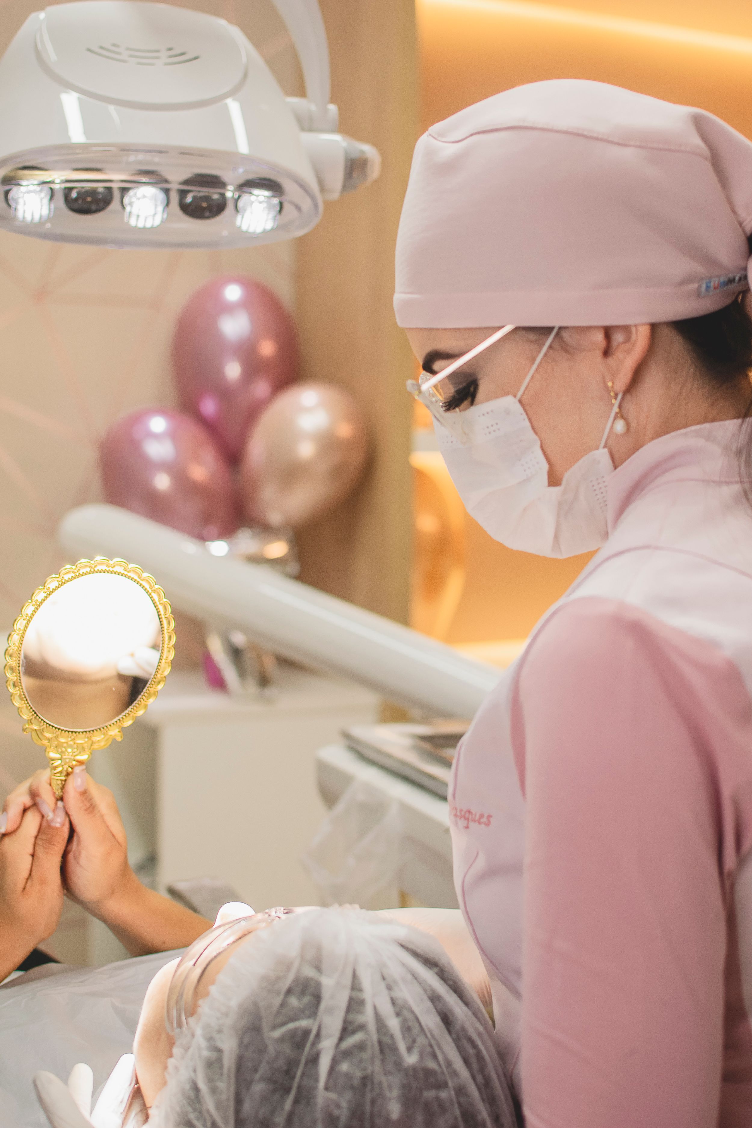 Dental professional in pink uniform holding a mirror during examination with pink balloons in the background.