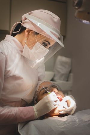 Dental practitioner wearing protective gear performing an oral examination on a patient.