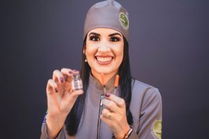 Healthcare worker in grey uniform holding medical tools against dark background.