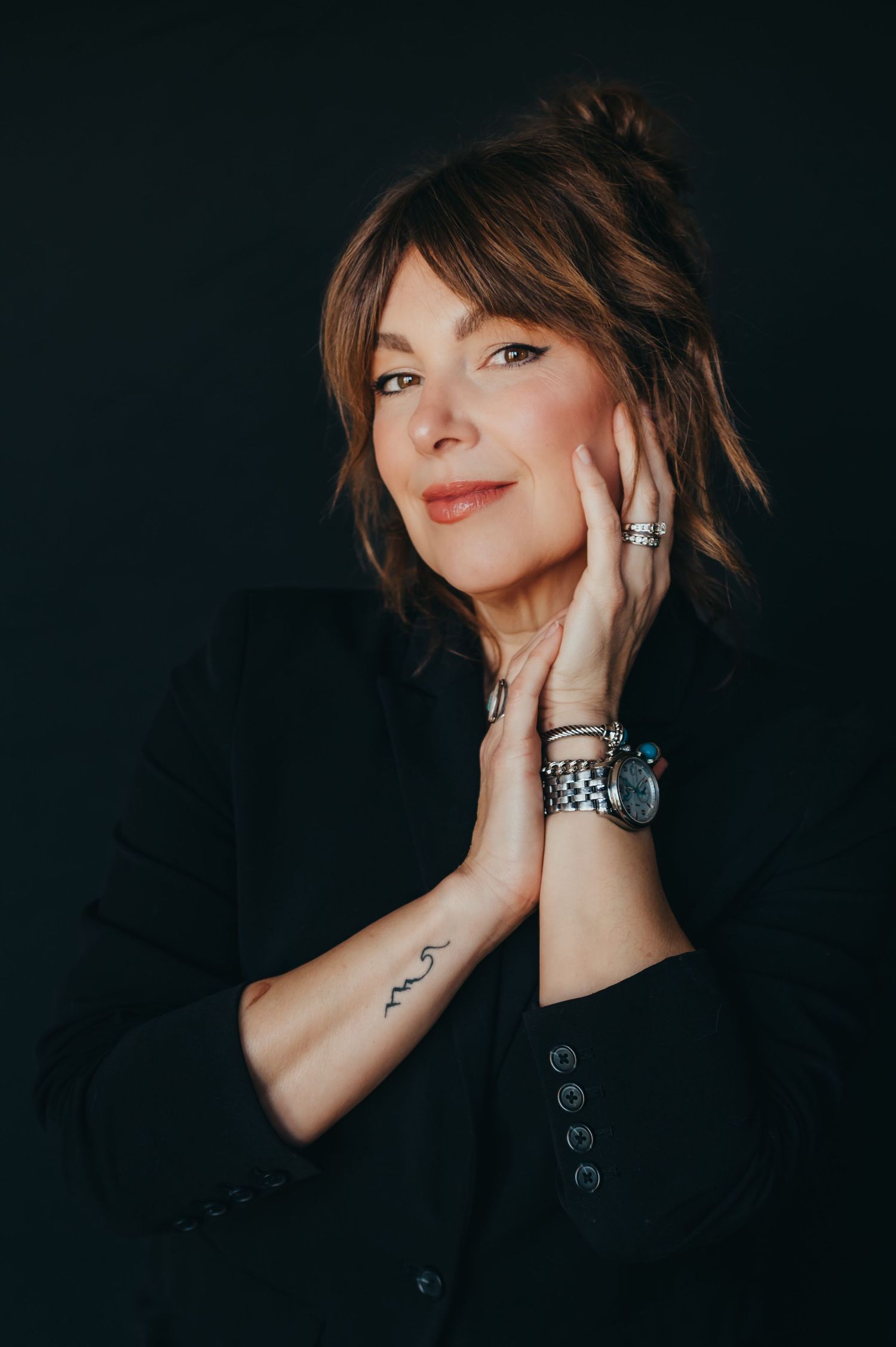 A professional portrait against a dark background featuring elegant jewelry and styling.
