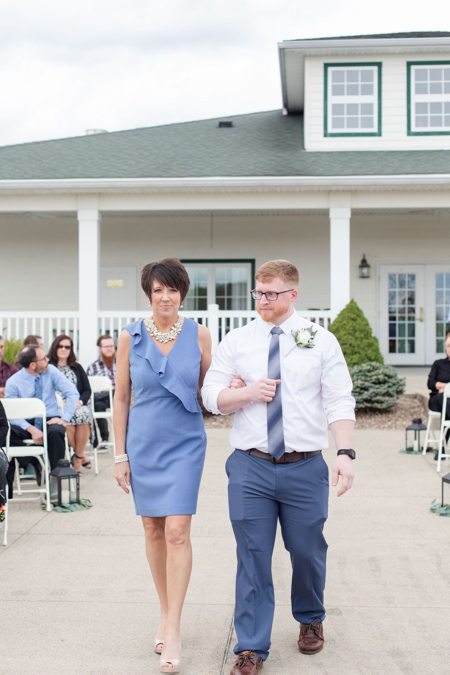 Wedding party members walking down the aisle outside a white clubhouse building.