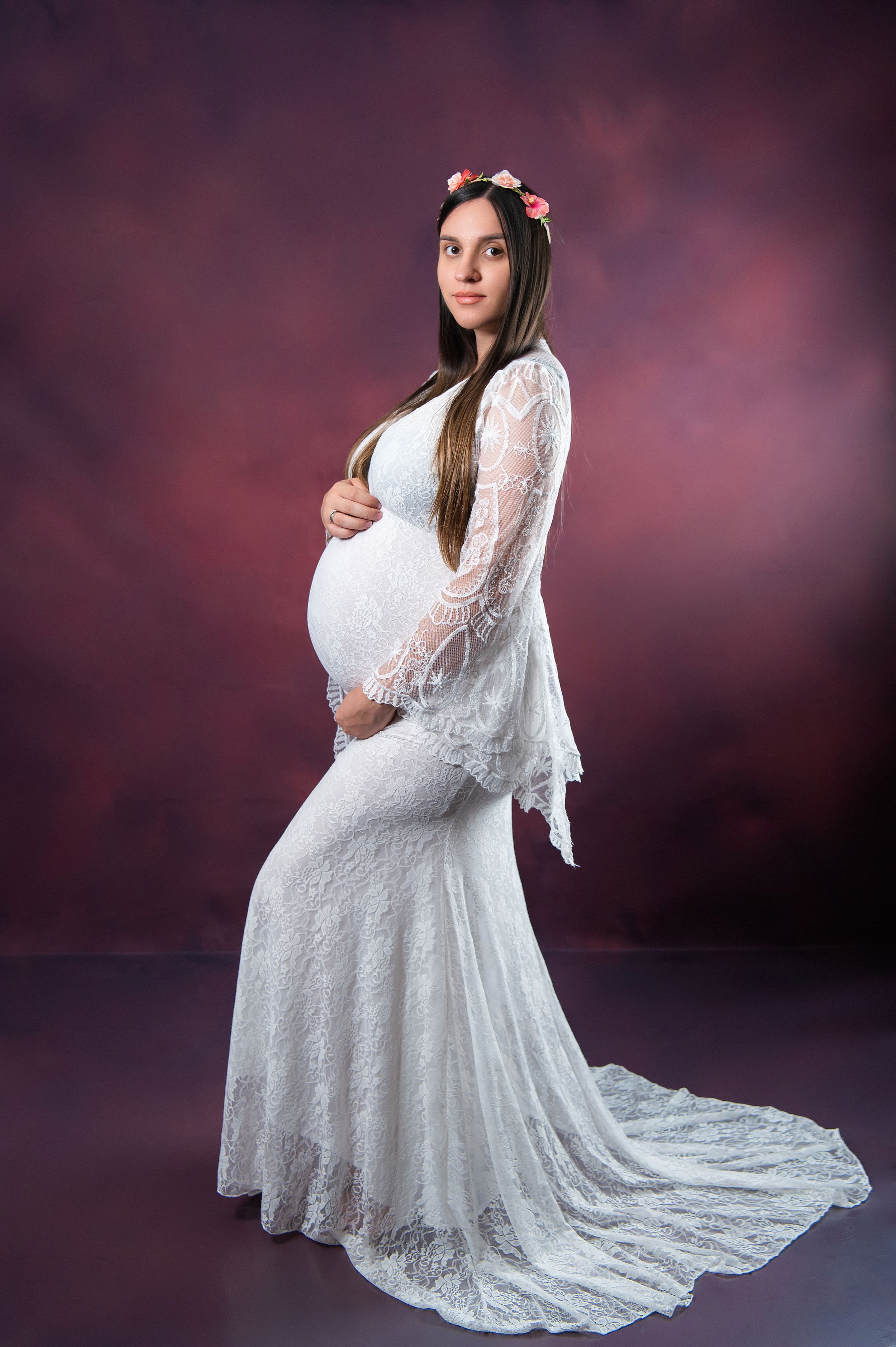 Elegant maternity photo featuring flowing white lace gown with train against moody background.
