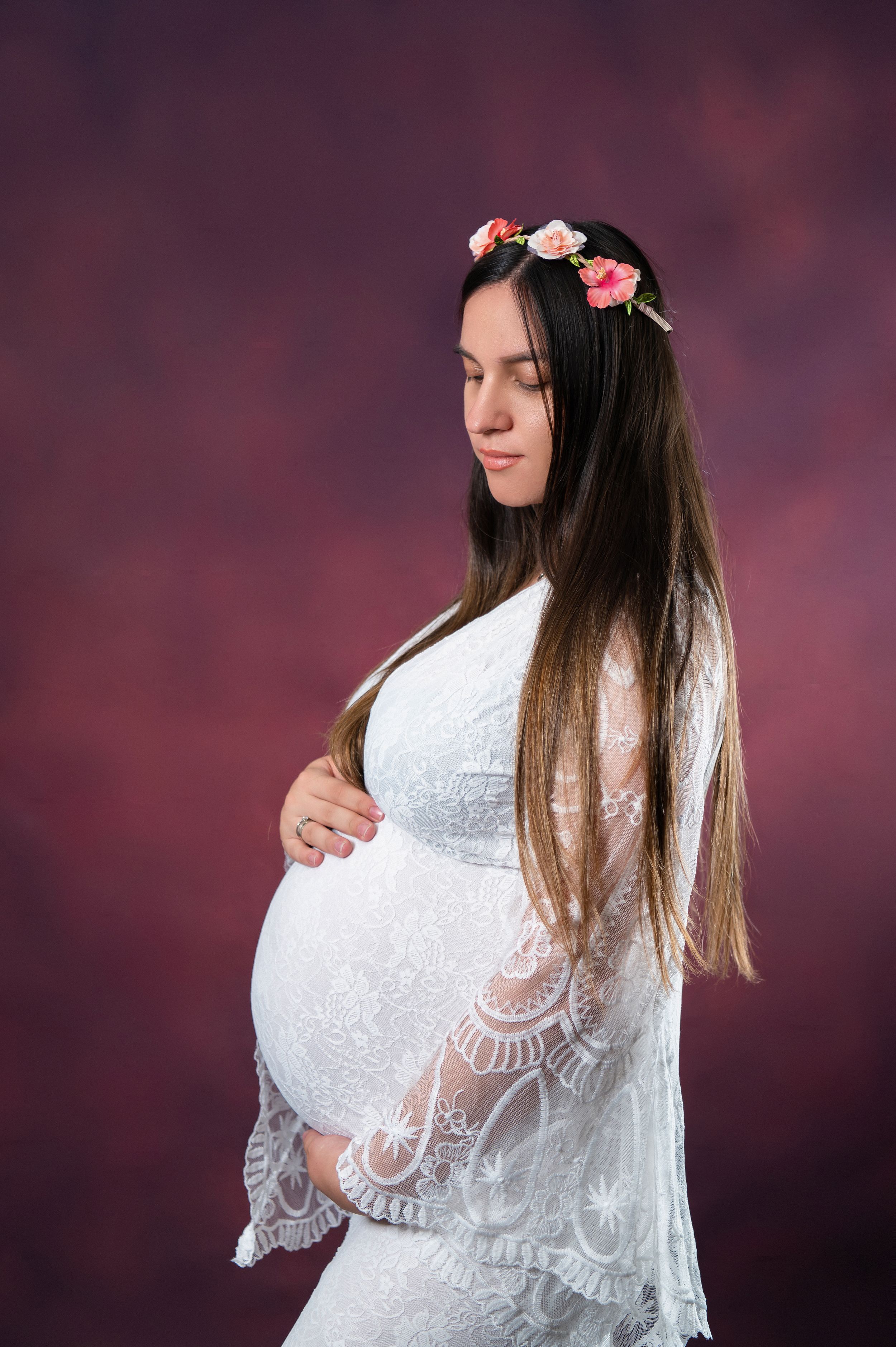Side view of maternity portrait in delicate white lace dress with floral hairpiece.