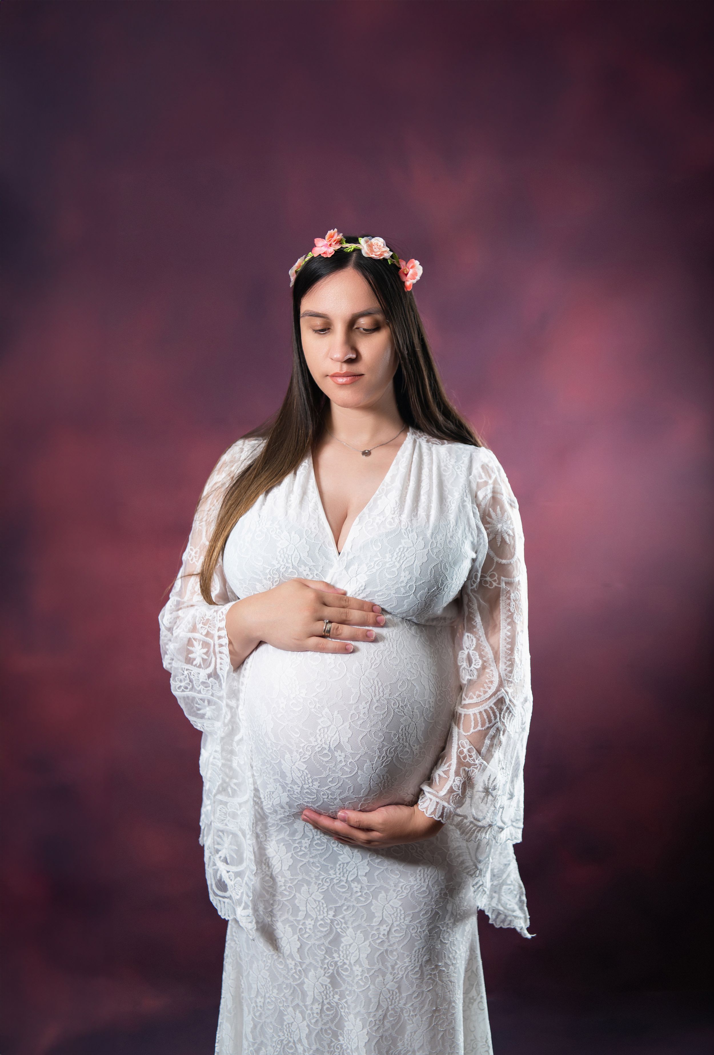 Intimate maternity portrait in white lace dress with hands cradling baby bump.