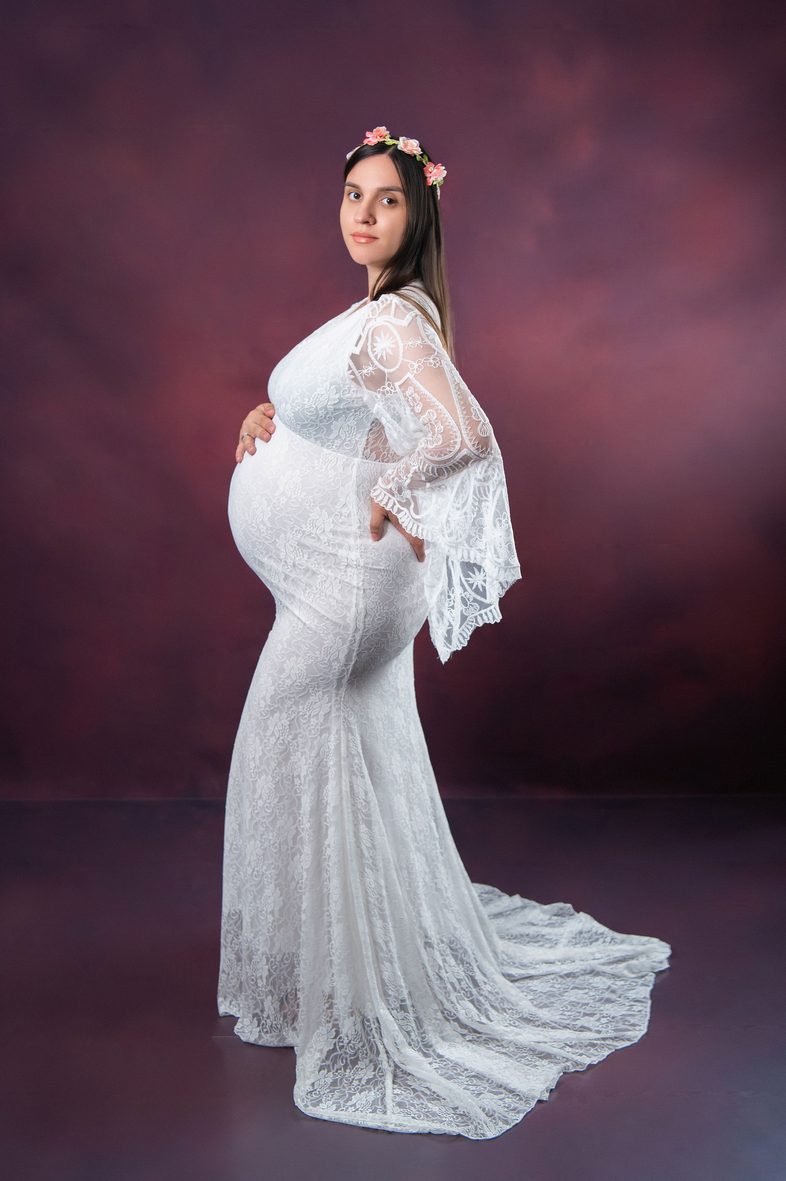 Artistic maternity portrait in white lace gown against deep purple background.