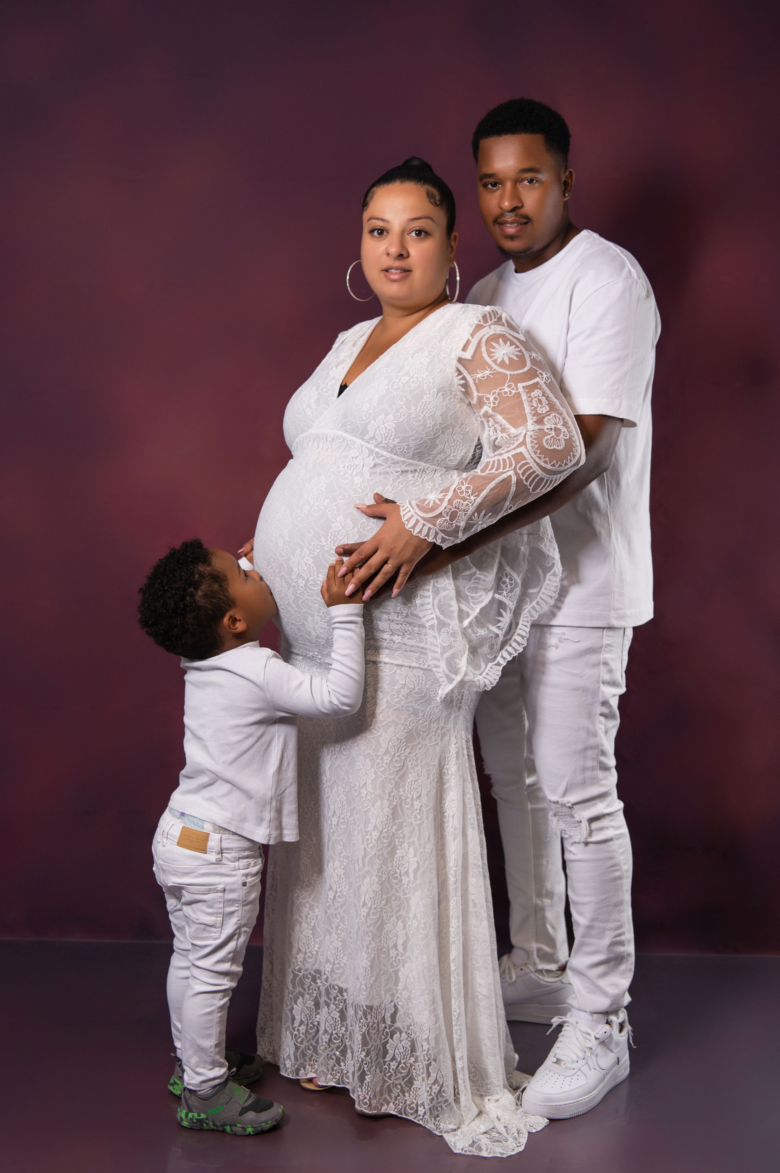 Family maternity session showing tender moments between child and pregnant mother in white lace dress.