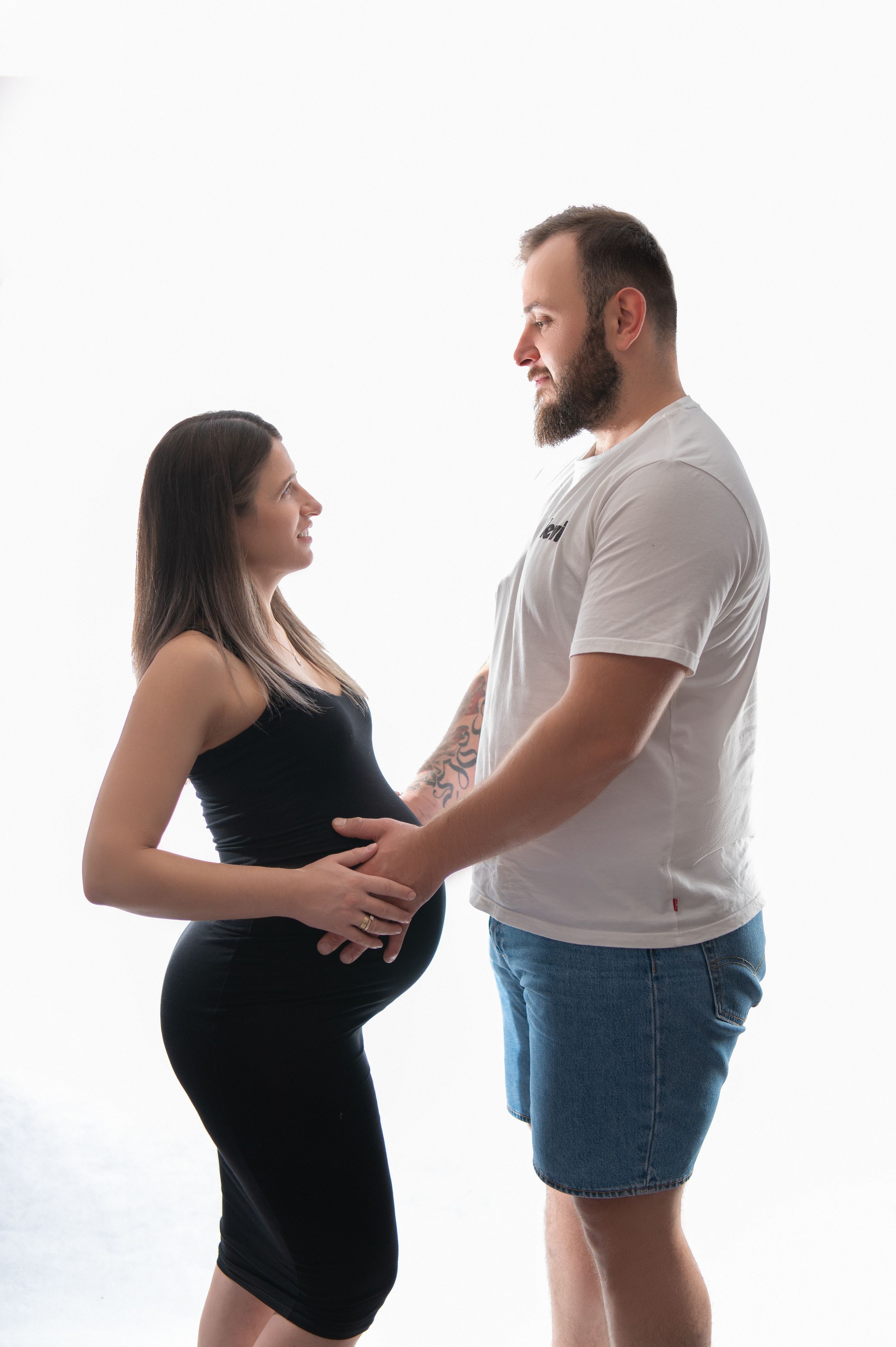 Intimate maternity photoshoot of couple sharing tender moments against white backdrop.