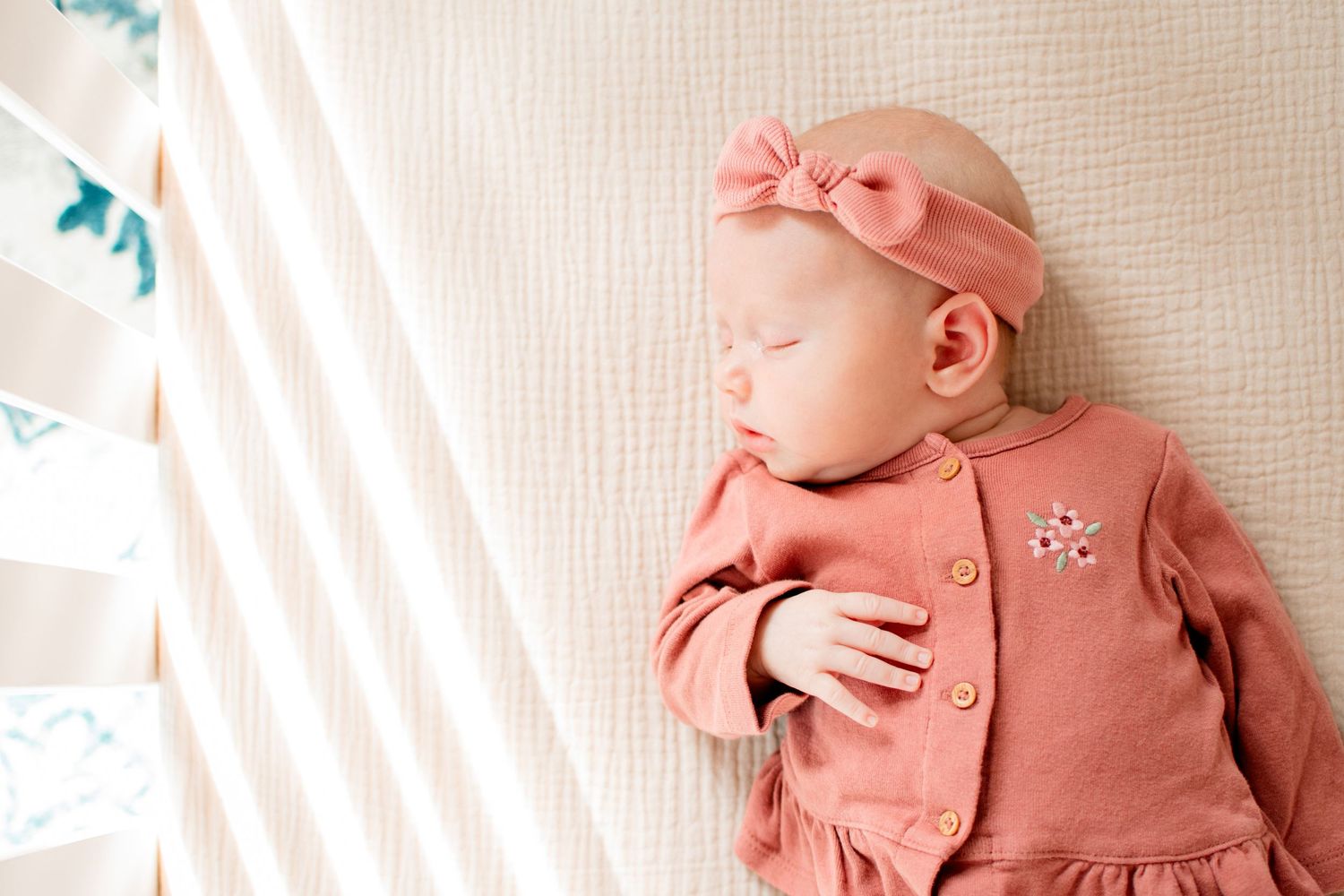Sleeping baby in coral outfit with matching headband on textured white bedding.