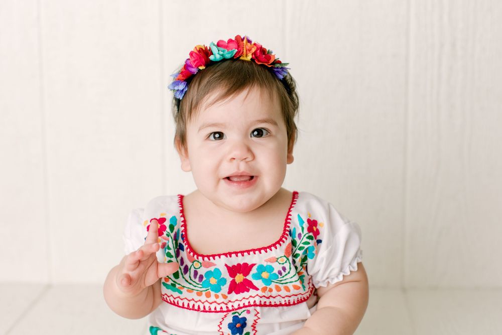 Baby in colorful Mexican-inspired outfit with floral crown smiling at camera.