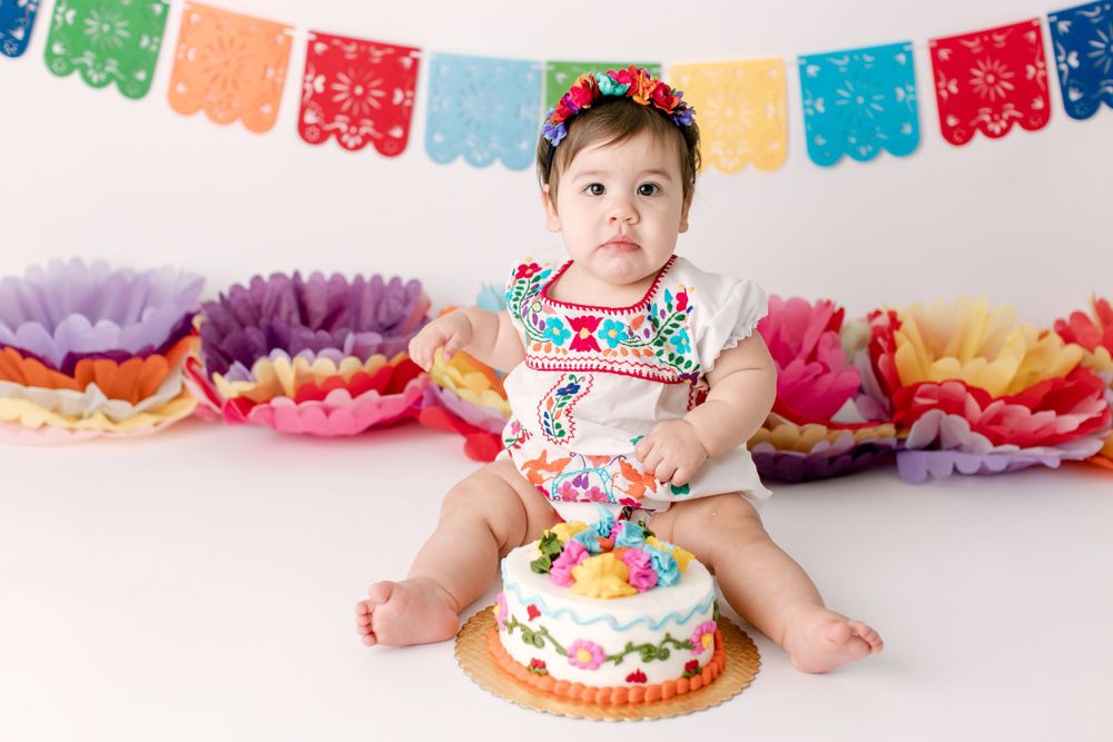 Baby in festive outfit with colorful bunting and cake for celebration.