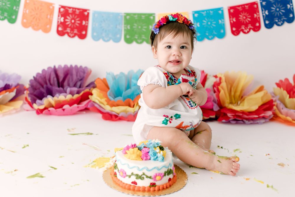Baby in embroidered romper with birthday cake and festive Mexican party decorations.